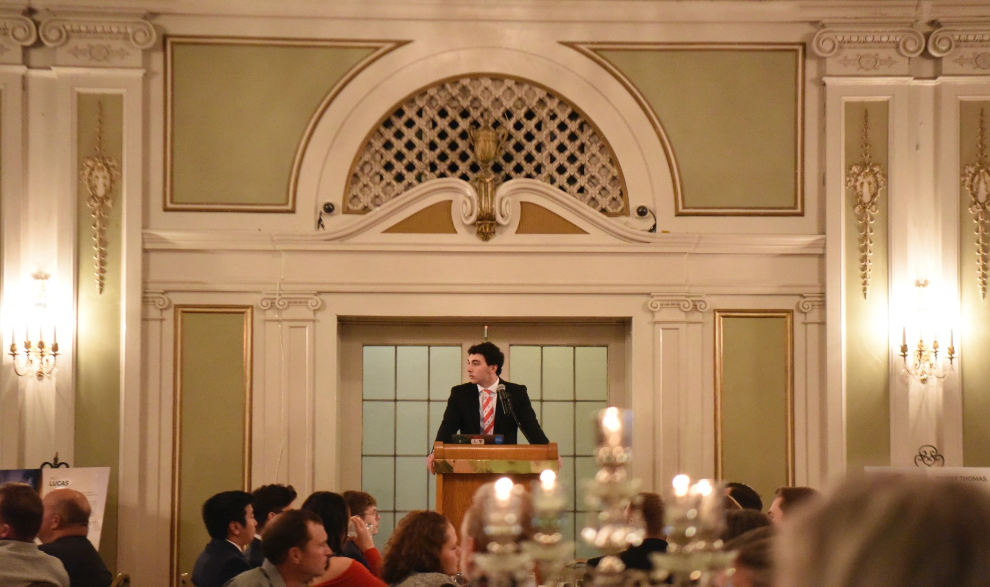 A brother speaking at the podium under the ballroom arch